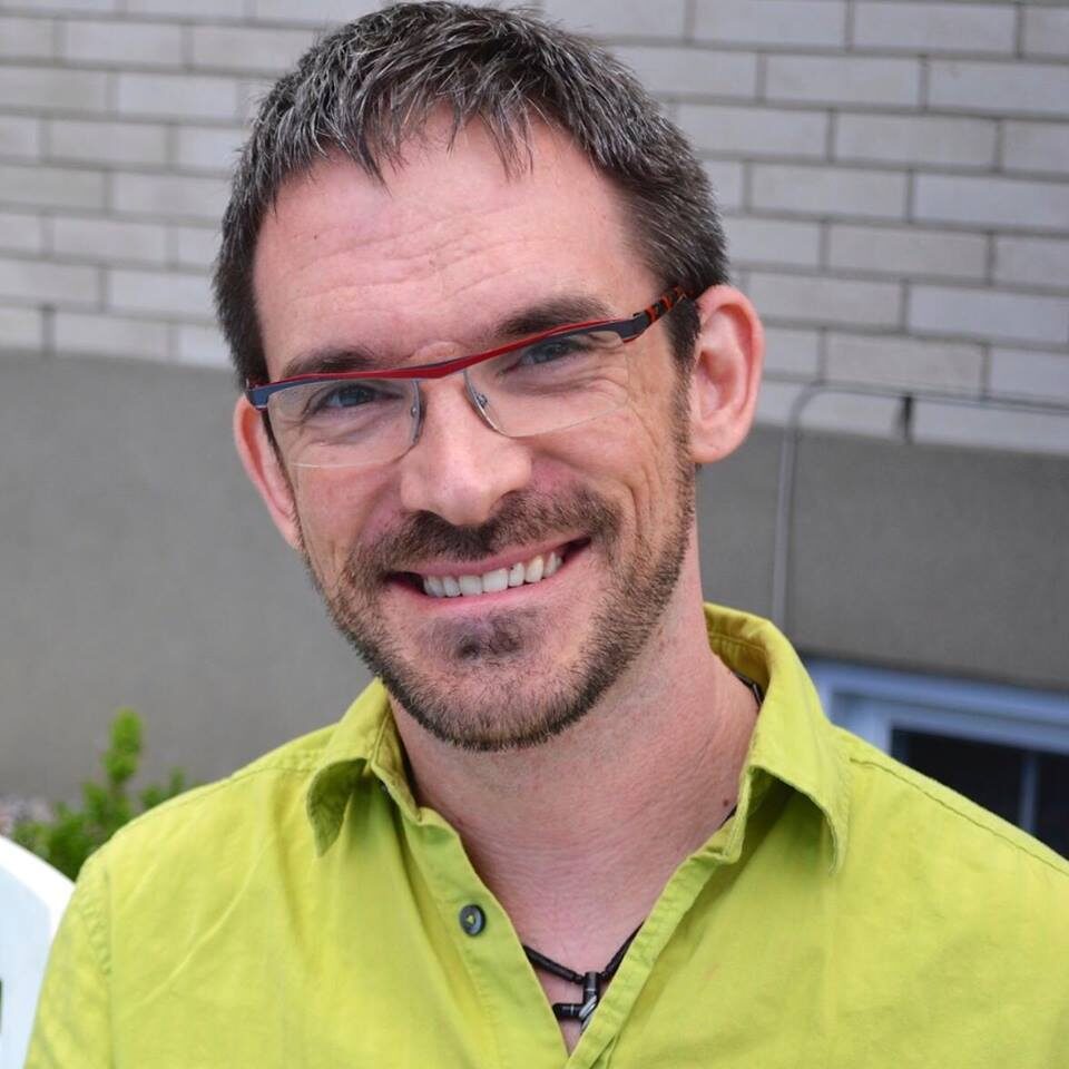 Smiling man with glasses and a green shirt.
