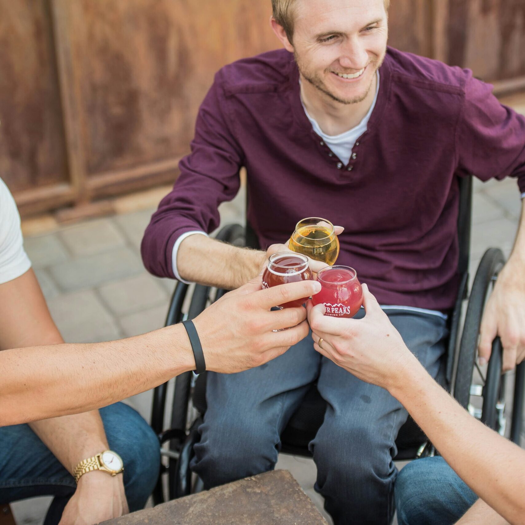 Three friends toasting drinks, one in a wheelchair, showcasing disability support.